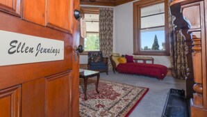 A room with a wooden door labeled "Ellen Jennings," a patterned rug, a blue armchair, a red sofa, and a window with a view of trees. - Dunstan House (Clyde)