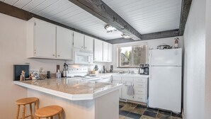 A kitchen with white cabinets, a central island with stools, a stove, and a refrigerator.