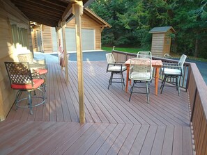 Eine Holzterrasse mit Gartenmöbeln, darunter Stühle und ein Tisch, sowie ein überdachter Bereich mit einem Fenster.