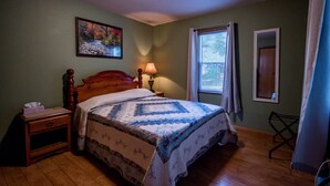 Une chambre à coucher avec un lit en bois, une table de chevet, une lampe de chevet, une fenêtre avec des rideaux et un tableau au mur.