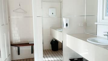 Un baño moderno con paredes de azulejos blancos, piso con patrón hexagonal, perchero, dispensador de jabón y cesto de basura.
