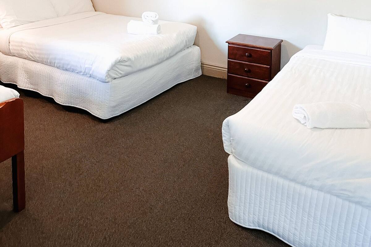 A hotel room with two beds, a wooden nightstand, and a small wooden table.