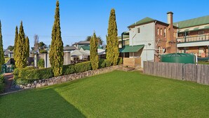 A residential area with a well-maintained lawn, tall cypress trees, and a brick building with a green roof. - Central Hotel Stroud (Stroud)