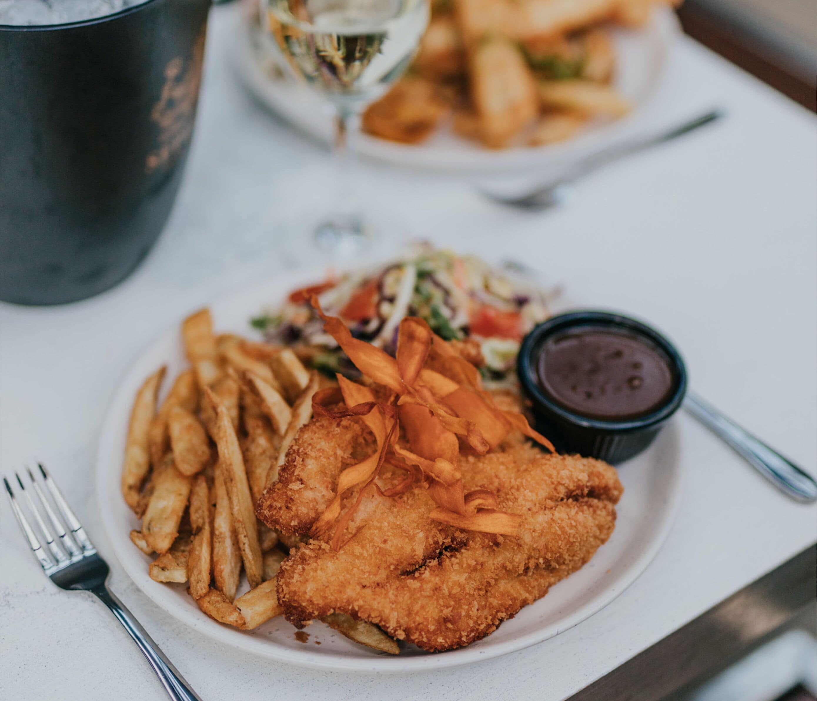 Une assiette de poisson frit, de frites et une salade, accompagnée d’un petit bol de sauce.