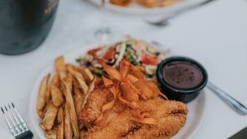 Une assiette de poisson frit, de frites et une salade, accompagnée d’un petit bol de sauce.