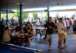 An outdoor dining area with multiple tables and benches, surrounded by a covered patio with a view of the hotel entrance. - Central Hotel Stroud (Stroud)