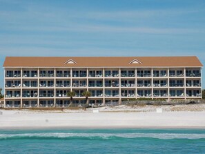 A multi-story hotel with balconies, located near a beach with a sandy shoreline and ocean waves.