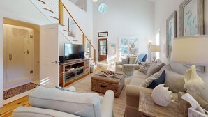 Un salón espacioso con techo alto, una escalera, un televisor y un área de estar confortable.