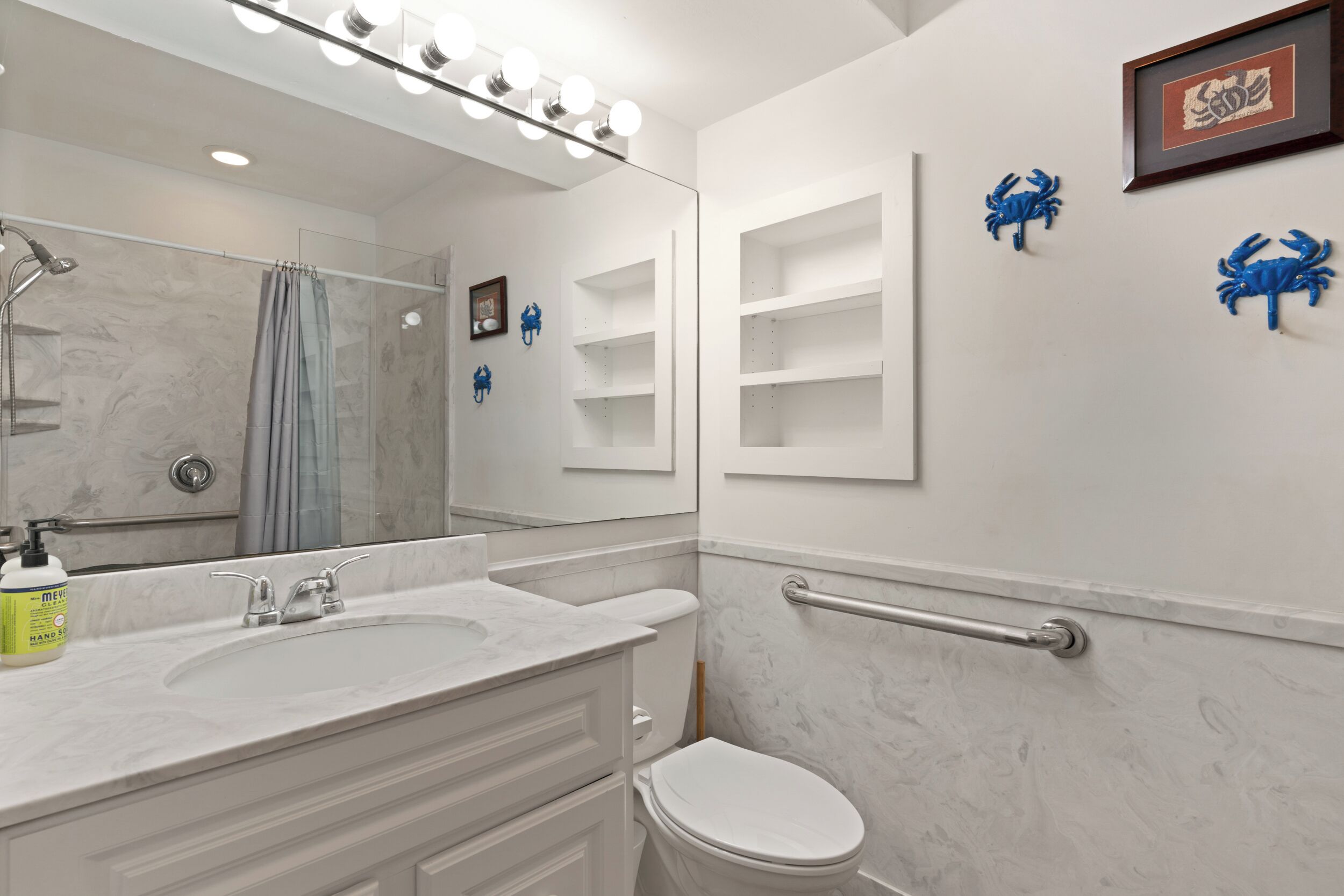 A bathroom with a white vanity, a sink, a mirror with lights, a shower, and a toilet.