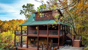A log cabin with a green roof, multiple balconies, and a view of a forested area.