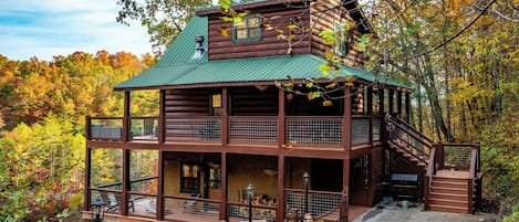 A log cabin with a green roof, multiple balconies, and a view of a forested area.