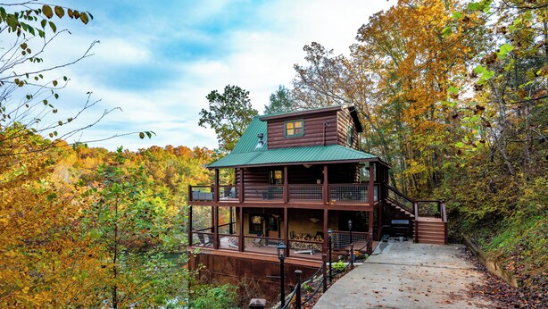 A log cabin with a green roof, a balcony, and a deck.