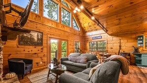 A cozy cabin interior with wooden walls, a fireplace, a sofa, and a dining area.