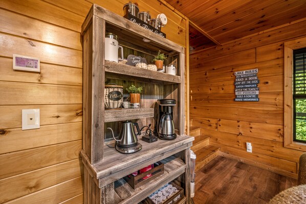 A wooden cabin interior with a coffee station, a thermostat, and a sign listing cabin rules.