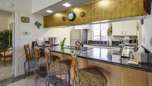 Uma cozinha com ilha central, banquetas, um relógio e diversos eletrodomésticos.