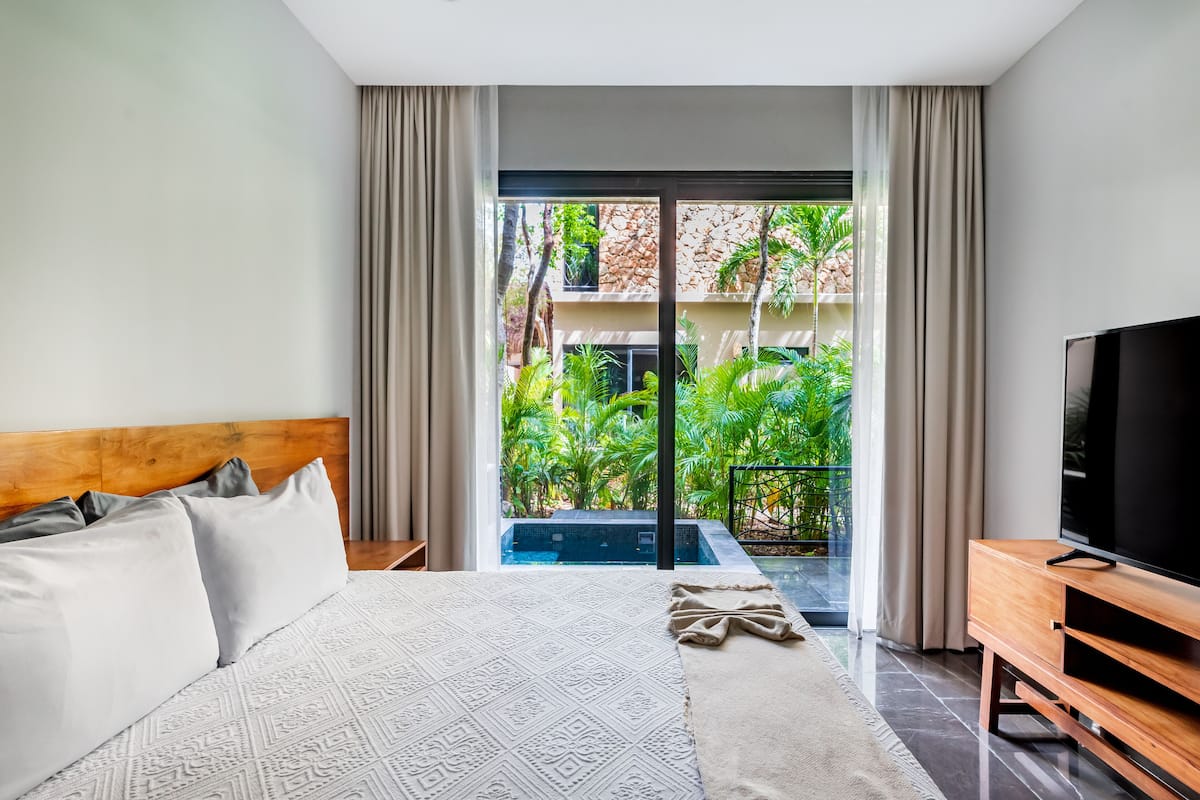 Habitación de hotel moderna con una cama grande, televisión y vistas a una piscina y zonas verdes.