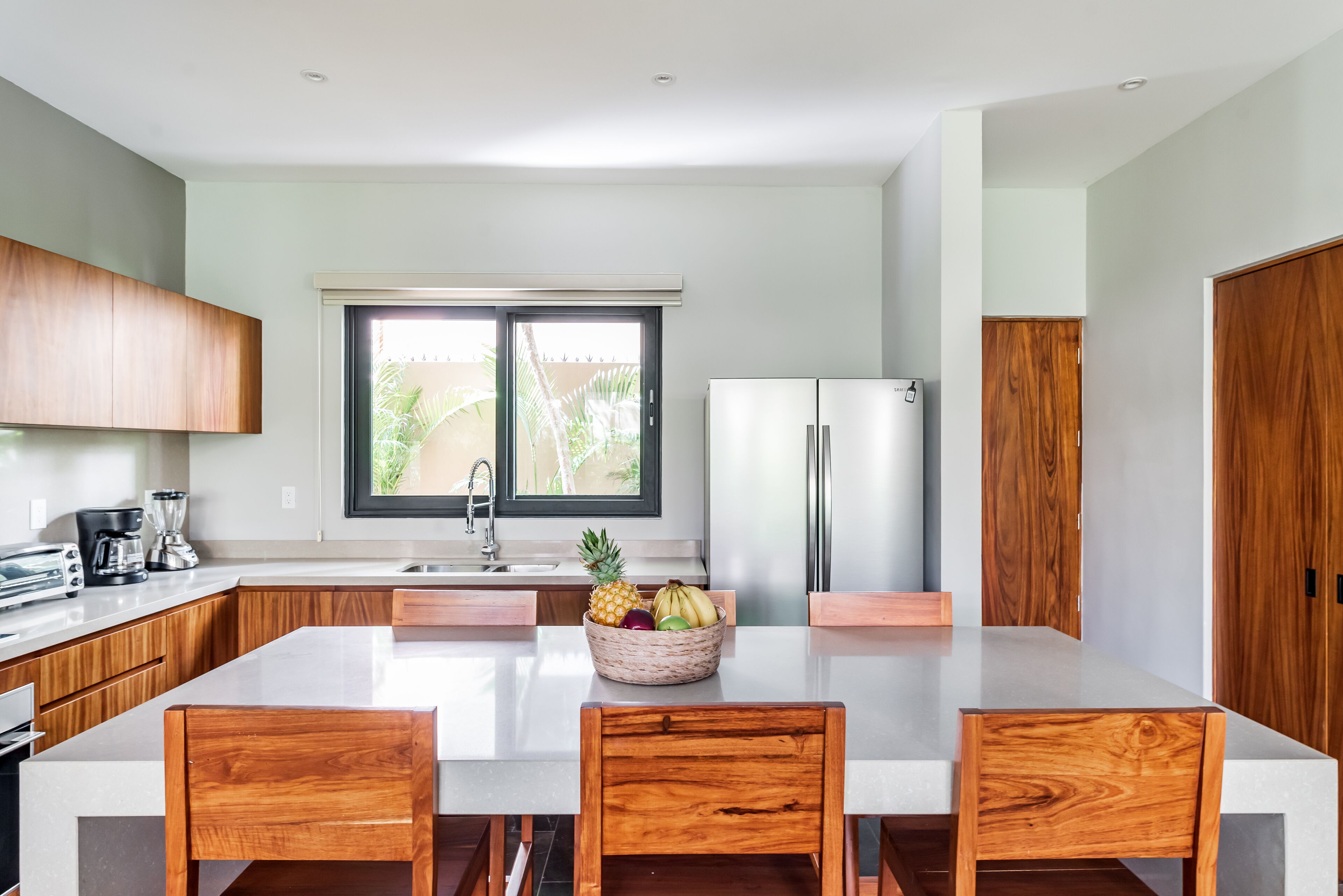 Een moderne keuken met houten kastjes, een groot kookeiland met een fruitschaal, en roestvrijstalen apparatuur.