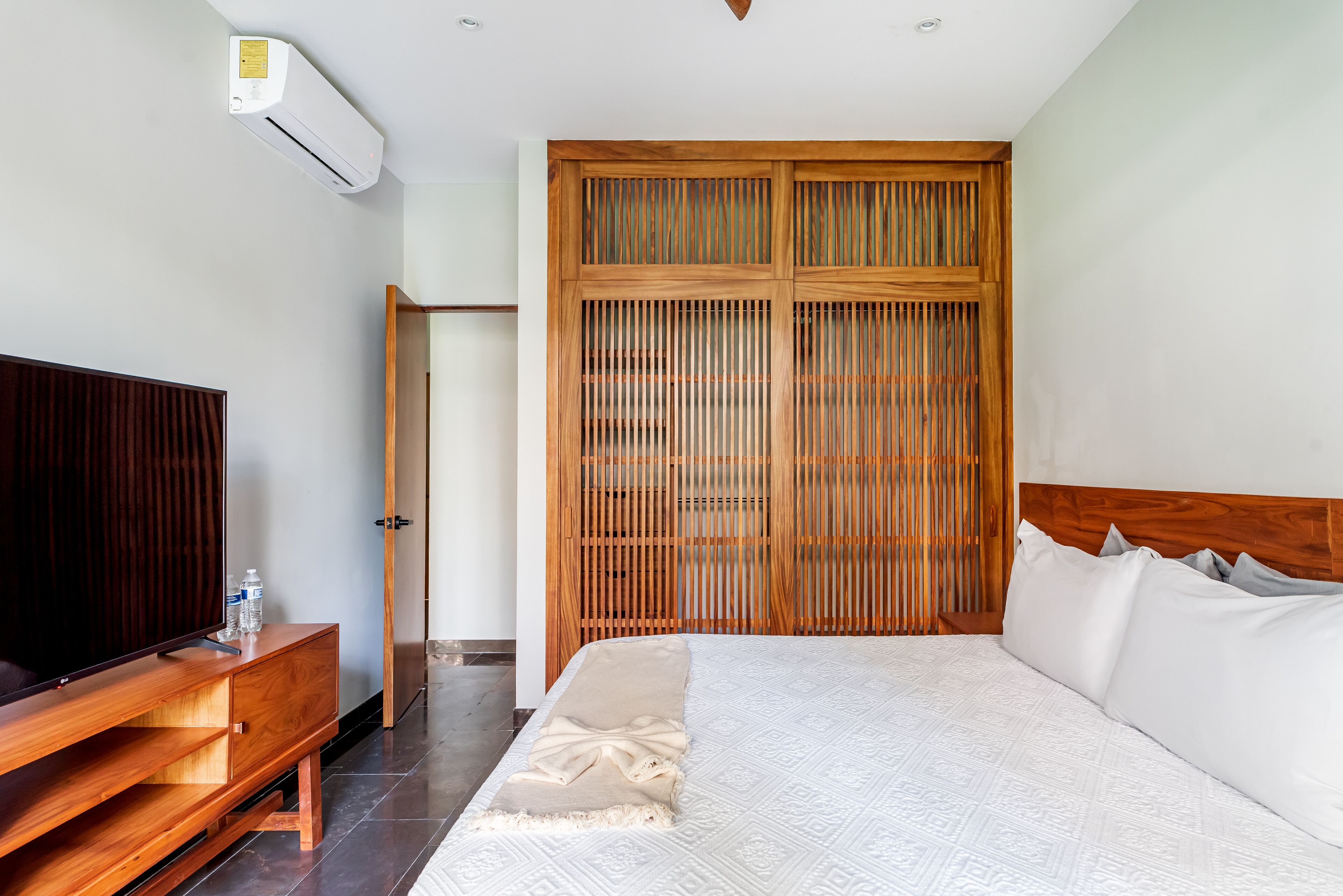 Un dormitorio con cama, un armario de madera, un televisor sobre un mueble de madera y un aire acondicionado en la pared.