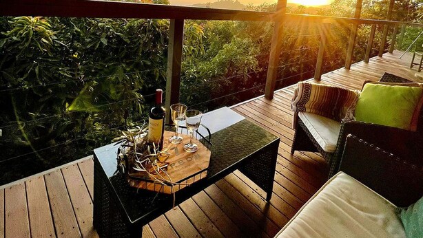 Una terraza de madera con una mesa, sillas, una botella de vino y una copa.