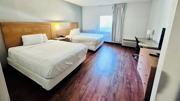 A hotel room with two beds, a desk with a lamp, a window with curtains, and a ceiling fan. - Studio 6 Extended Stay - Savannah, GA - Gateway & I-95 (Savannah)