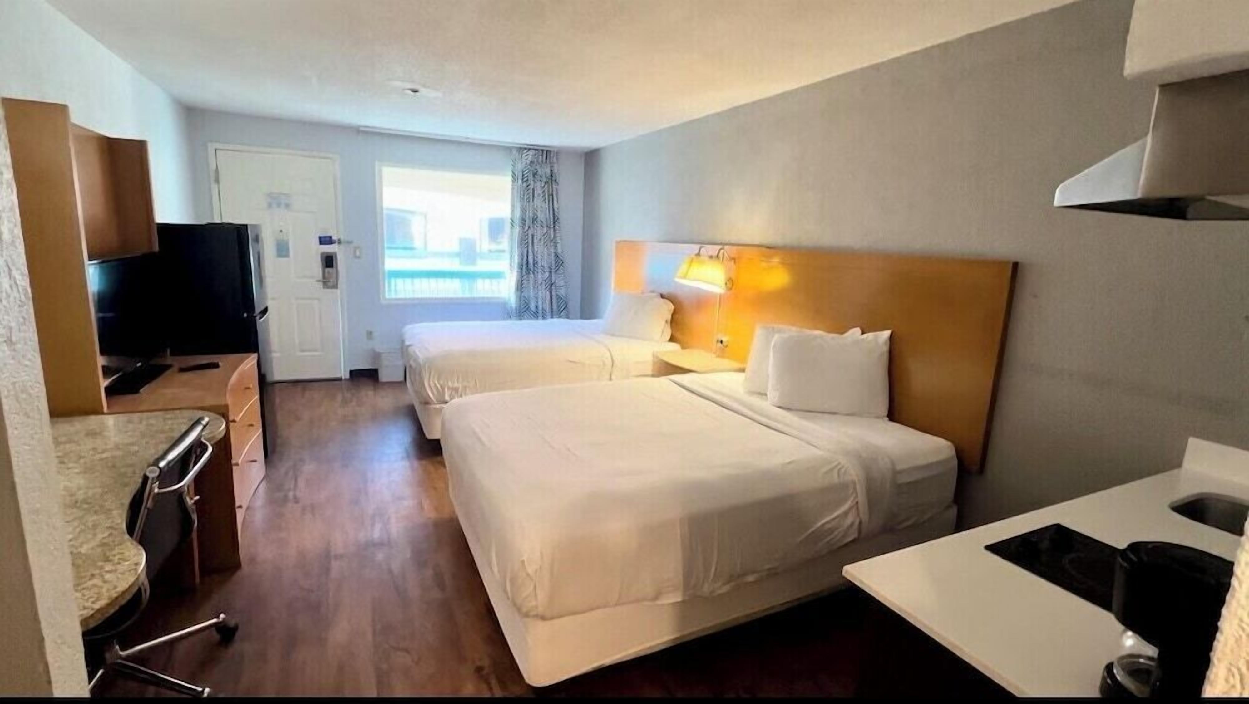 A hotel room with two beds, a desk, a television, and a window with curtains.