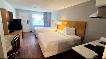 A hotel room with two beds, a desk, a television, and a window with curtains.