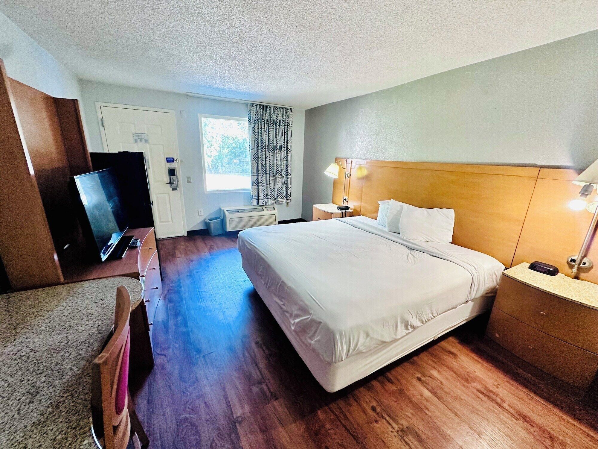 Une chambre d’hôtel avec un grand lit, un bureau avec un ordinateur, une télévision et une fenêtre avec des rideaux.