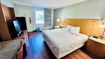 A hotel room with a large bed, a desk with a computer, a TV, and a window with curtains.
