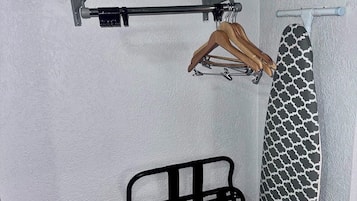 A small room with a metal drying rack, a wooden hanger, and a patterned ironing board.