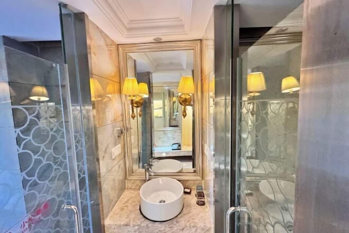 Un baño moderno con un lavamanos redondo, cabina de ducha de vidrio y un espejo con apliques de pared.