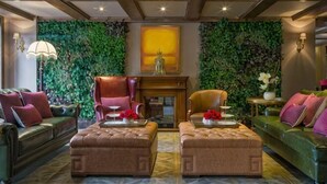 A room with a green leafy wall, a fireplace, two ottomans, a sofa, and a chair. - Cannes City Hotel (Luzhou)
