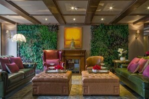 A room with a green leafy wall, a fireplace, two ottomans, a sofa, and a chair. - Cannes City Hotel (Luzhou)