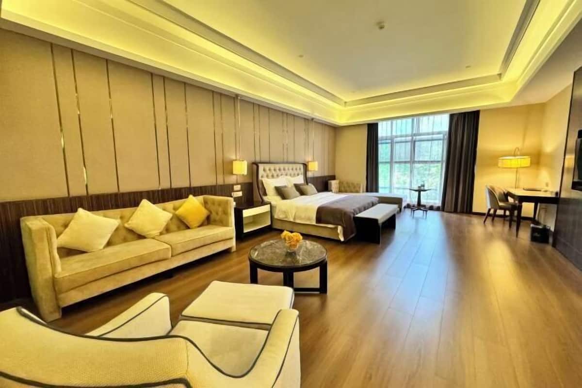 Habitación de hotel con cama, sofá, sillón y una mesita con un florero.