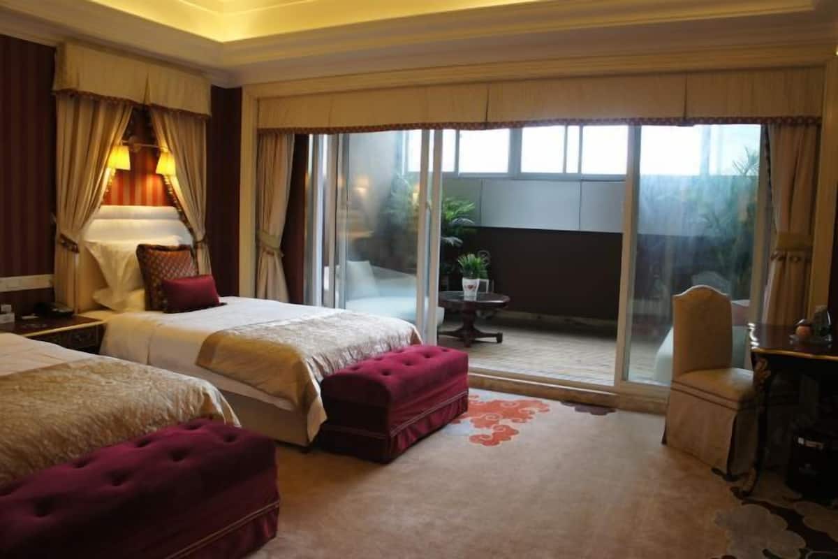 Habitación de hotel con dos camas, una sala de estar con mesa y sillas, y una puerta corrediza de vidrio que da a un área exterior.