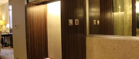 A hotel room with a wooden wardrobe, a small table with a box and papers, and a mirror with a wooden frame.