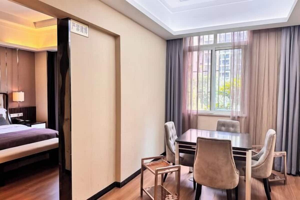 Habitación de hotel con cama, mesa de comedor con sillas, ventana con cortinas y un cartel en la pared.