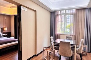 A hotel room with a bed, a dining table with chairs, a window with curtains, and a sign on the wall.