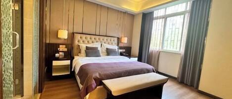 A modern hotel room with a large bed, bedside tables, a bench, and a large window.