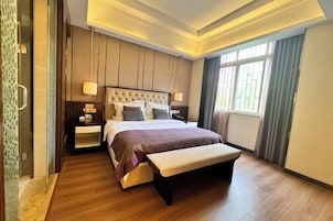 Una habitación de hotel moderna con una cama grande, mesitas de noche, un banco y un ventanal amplio.