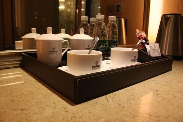 A tray with two white cups and a teapot, a spoon, and a small figurine on a marble countertop.