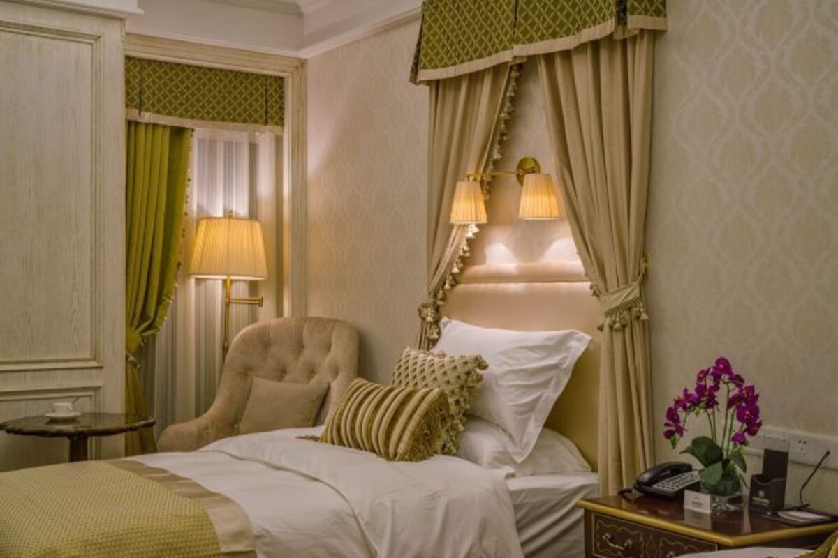 A hotel room with a bed, a chair, a nightstand, and a lamp.