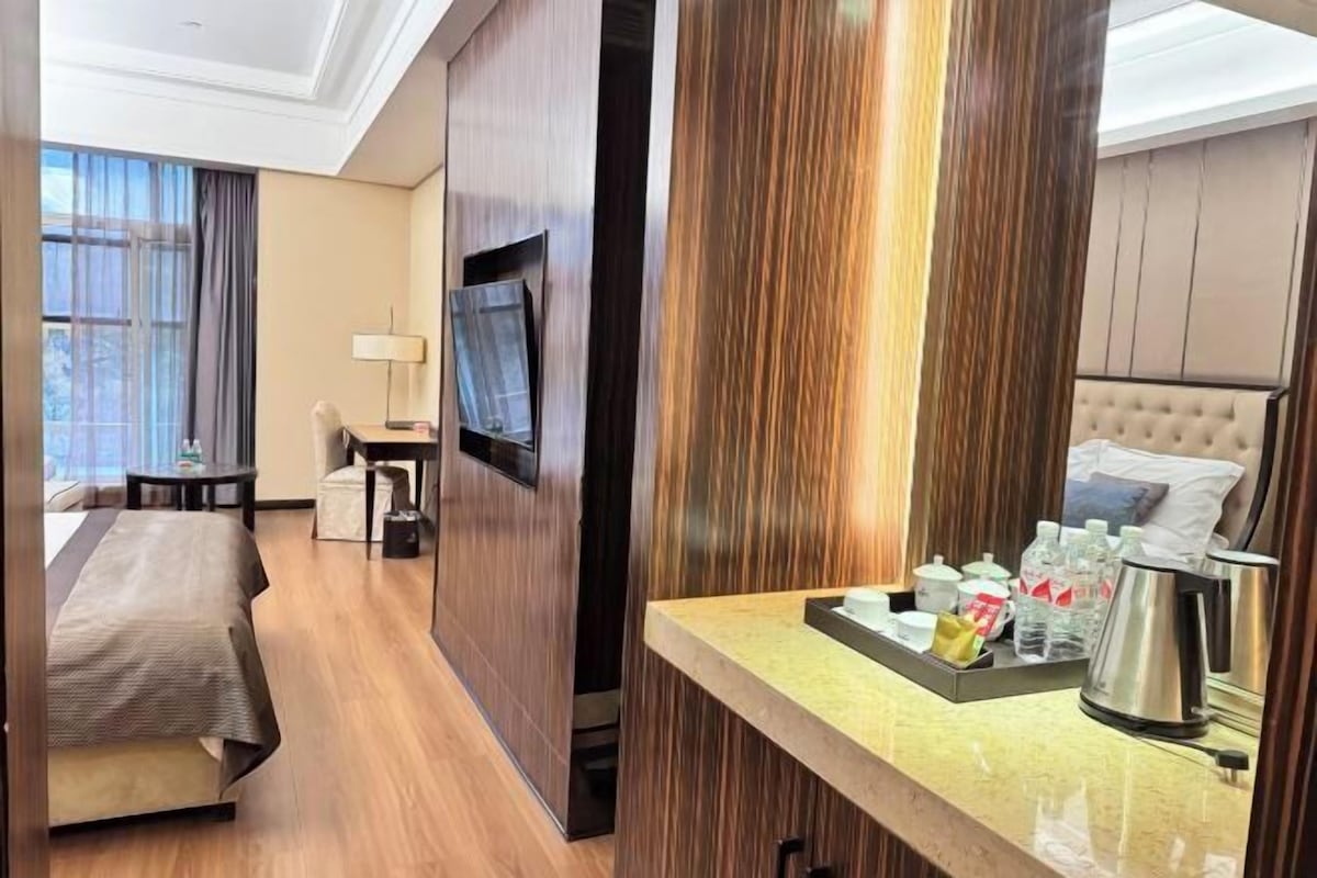 A hotel room with a bed, a desk, a TV, and a breakfast tray with coffee and snacks.