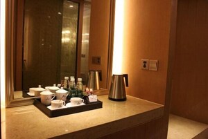 Un baño de hotel con un espejo, una bandeja de artículos de aseo, una cafetera y una lámpara.