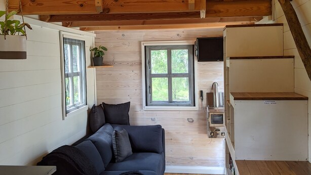 A compact cabin with a loft bed, a sofa, and a staircase.