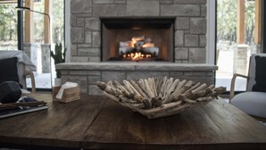 A stone fireplace with a fire, a wooden bowl with driftwood on a table, and a chair.