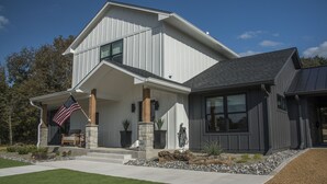 A modern two-story house with a covered front porch, stone pillars, and an American flag.