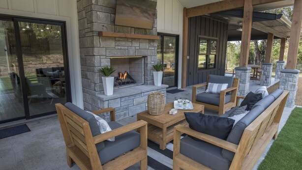 A covered outdoor seating area with stone walls, a fireplace, and wooden furniture.