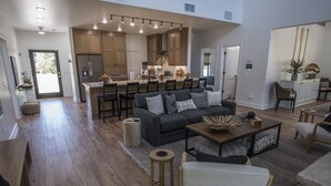 A spacious living area with a dark grey sofa, wooden coffee table, and a kitchen in the background.