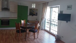 Un comedor con mesa y sillas de madera, una cocina verde con estufa y un ventanal con vista a un balcón.
