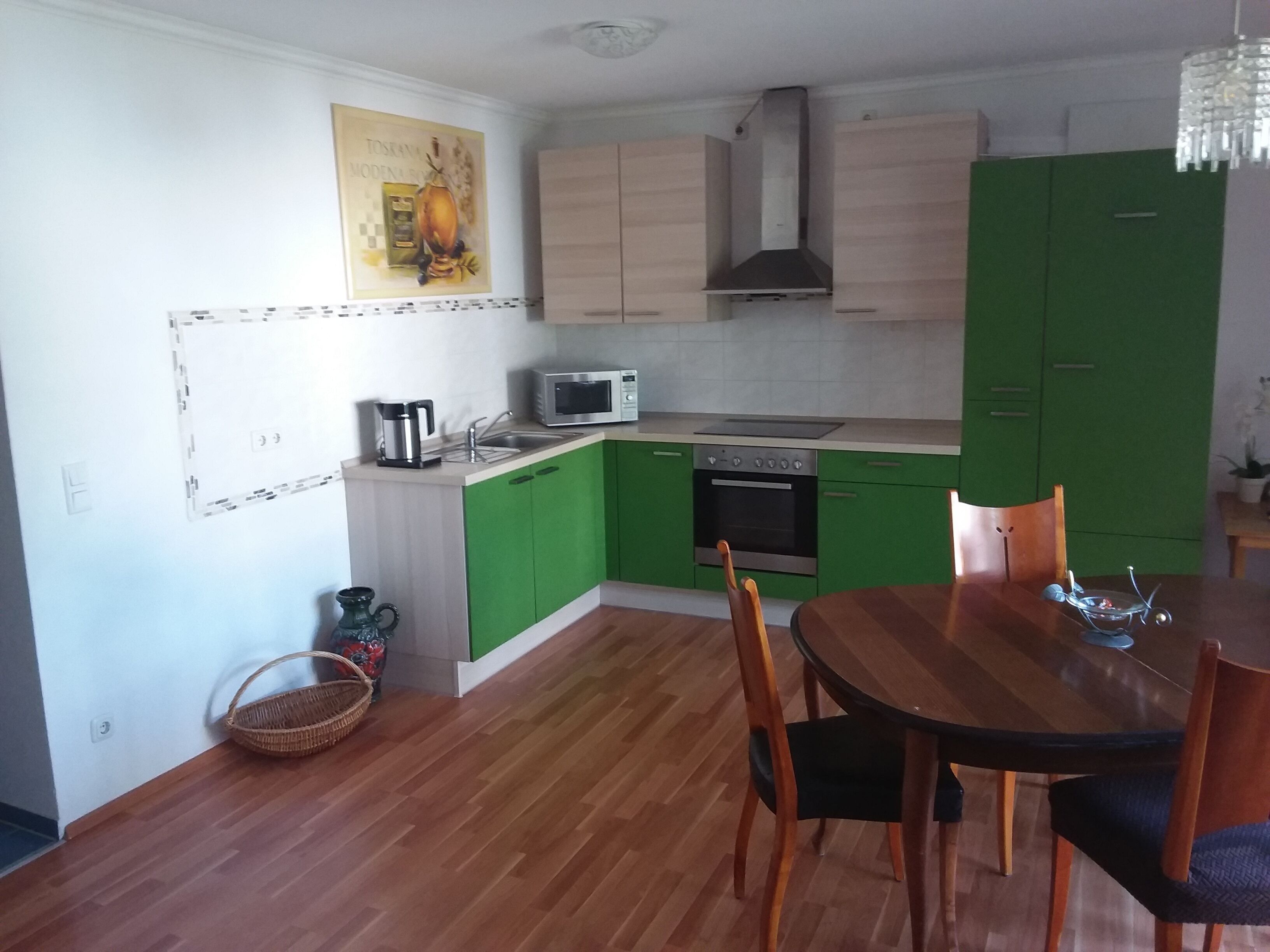 Eine kompakte Küche mit grünen Schränken, einer Mikrowelle, einem Backofen und einem Essbereich mit Tisch und Stühlen.